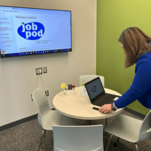 woman at table using laptop with JobPod information on wall monitor